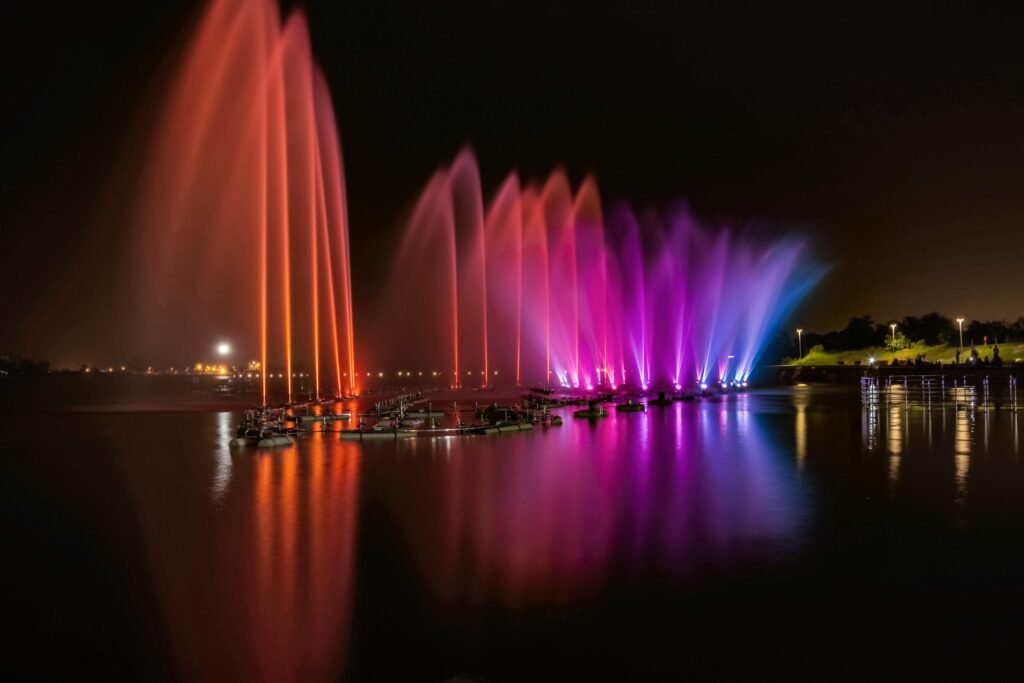 Vibrant fountain display with colorful lights reflecting on a river at night in the city.