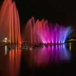 Vibrant fountain display with colorful lights reflecting on a river at night in the city.